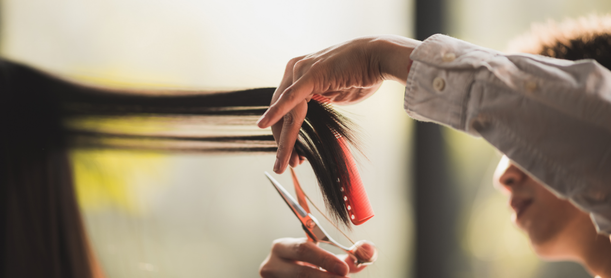 美容師がハサミとコームを使って女性の長い髪をカットしている様子